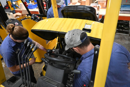 Close-up of two technicians performing hands-on maintenance on a Hyster forklift.